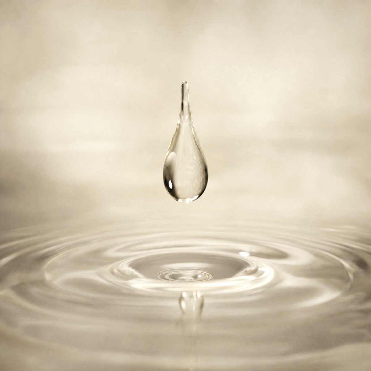 A single clear droplet suspended above still water